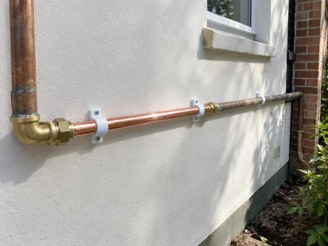 Repaired copper water pipe on an external rendered wall beside a window in Mayfield