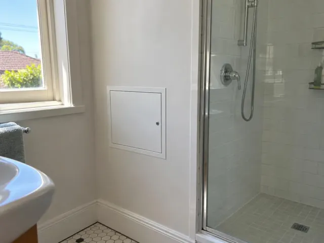 Bathroom wall with a small access panel beside a shower and window in Georgetown