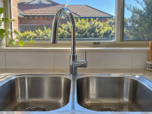 Chrome mixer tap over double stainless kitchen sink with tiled splashback and window in Waratah