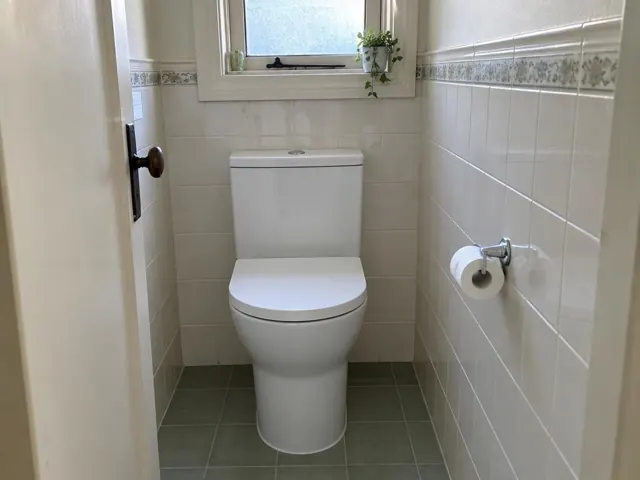 White toilet in a small tiled bathroom with frosted window and tiled walls in Waratah